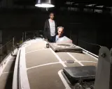 Nicole Van de Kerckhove et un autre homme sur le pont d'un voilier dans un hangar sombre.