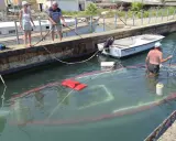 Un bateau accidenté est partiellement submergé dans un port. Des personnes sur le quai tentent de gérer la situation.