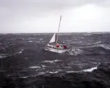 Un voilier affronte une mer agitée, sa voile blanche tendue. La mise à la cape est une manœuvre de survie face aux éléments déchaînés.