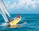 Un voilier jaune fend les vagues bleues, ses voiles blanches gonflées par le vent. L'équipage profite de cette belle journée pour faire la voile.