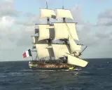 La frégate Hermione, fierté de la marine française, navigue majestueusement sur l'océan, ses voiles gonflées par le vent.