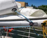 Le cordage bleu passe dans un œillet de la voile, prêt à ajuster la bosse de ris. Une amarre jaune est enroulée sur un taquet.