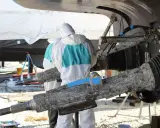 Travailleurs en combinaison protègent un bateau aluminium contre l'électrolyse. Des pièces rouillées sont visibles.