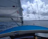 Vue depuis un voilier, avec la liste des voiles d'un bateau gonflées par le vent. La mer est agitée sous un ciel nuageux.