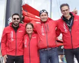 Erwan Thiboumery et trois autres personnes souriantes portent des vestes rouges du Groupe Interaction, devant un bateau.