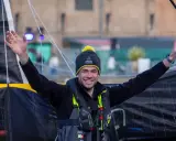 Nicolas d'Estais, marin souriant, bras levés, porte un bonnet et un gilet de sauvetage, prêt pour l'aventure en mer.