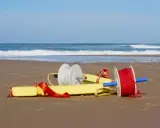 Deux bobines de fil, une blanche et une rouge, sont attachées à un tube de sauvetage jaune sur une plage.