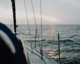 Vue depuis le pont d'un voilier insubmersible naviguant sur une mer calme au coucher du soleil.
