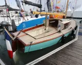 Un élégant belouga bateau, aux finitions bois et coque turquoise, est amarré à quai.
