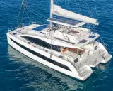 Un catamaran blanc, une véritable bicoque bateau, navigue sur une mer bleue. Ses voiles sont partiellement déployées, et des panneaux solaires brillent sur son toit.