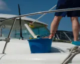 Un homme effectue l'entretien de bateau, lavant la proue avec une brosse et un seau bleu.