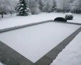Piscine recouverte d'une couverture blanche et etanche, dans un jardin enneigé. Le paysage hivernal est paisible.