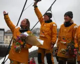 Des femmes en cirés jaunes célèbrent la fin du célèbre projet, bouquets à la main.