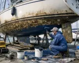 Un marinier applique une nouvelle couche de peinture antifouling sur la coque d'un voilier. Il est temps de choisir quel antifouling choisir pour protéger le bateau.