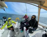 Équipage souriant sur un voilier, profitant de la navigation. Personne n'a besoin d'écoper, la mer est calme.