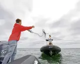 Un jeune homme lance une corde pour le remorquage d'un bateau en panne. Une femme attend sur l'autre embarcation.