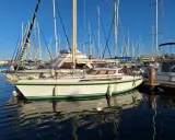 Un voilier blanc et vert, un Jeanneau Espace 1000, reflète sur l'eau calme d'un port.