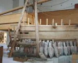 Amphores antiques alignées devant une reconstitution de navire en bois, rappelant le transport de vin par un ancien pinardier.