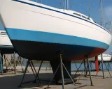 Vue rapprochée de la coque d'un voilier blanc avec une bande bleue et une bande rouge. Le choix couleur coque bateau est important pour l'esthétique.