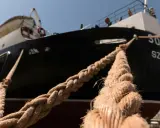 Gros plan sur des cordages épais assurant l'amarrage d'un bateau noir et blanc, avec des bâtiments colorés en arrière-plan.