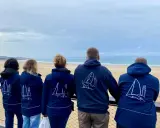 Cinq personnes portent des vestes bleues avec des voiliers dessinés. Benoit Marie et ses amis admirent la mer.