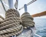 Gros cordages enroulés sur des taquets, prêts pour l'aventure. La proue du bateau fend les flots bleus sous un ciel clair.