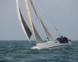 Équipage sur un voilier blanc, le foc et le génois gonflés par le vent, naviguant sur une mer agitée.