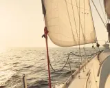 Voile de bateau gonflée par le vent, naviguant sur une mer calme au coucher du soleil.