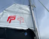 Voile blanche avec logo rouge, prête à naviguer à la voile sous un ciel bleu.