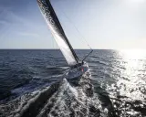 Voilier Banque Populaire naviguant au soleil, l'eau éclabousse le long du babord tribord.