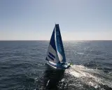 Voilier bleu et blanc "Inter Invest" naviguant sur une mer calme. Matthieu Perraut, skipper, est à la barre.