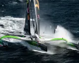 Le trimaran Sodebo, un bateau ultime, fend les vagues sombres, projetant des gerbes d'eau dans une course effrénée.