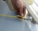 Main d'un marin préparant la ligne de vie d'un voilier, sécurisant une amarre sur un taquet.