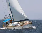 Un voilier blanc navigue sur une mer bleue agitée. L'équipage semble prendre un ris, ajustant les voiles pour mieux affronter le vent.