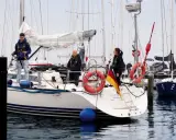 Trois personnes sur un bateau, prêtes à appareiller. Le drapeau allemand flotte fièrement. L'erre bateau est calme.