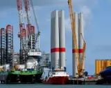 Un navire jack-up avec des grues massives se tient à côté de grandes tours d'éoliennes, prêt pour l'installation.