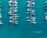 Vue aérienne d'un port où de nombreux voiliers sont amarrés. Un petit bateau navigue, laissant une trace dans l'eau. Le **bloc côtier obligatoire** est bien visible.
