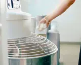 Main d'un boulanger ajoutant de la pâte à un pétrin, partie intégrante de l'entretien du matériel en cuisine.
