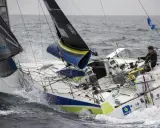 Un skipper navigue sur un voilier blanc et bleu, affrontant les vagues. Le nom "Pierre Quiroga" est visible sur la coque.