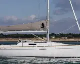 Voilier blanc "First 25 Performance" naviguant sur une mer calme, avec une voile grise arborant un logo noir.