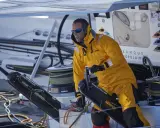 Skipper en tenue jaune, concentré, manœuvre un winch sur un bateau Banque Populaire.