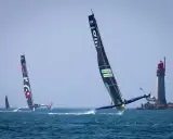 Course d'Ocean Fifty près d'un phare. Les trimarans filent sur l'eau, leurs voiles noires portant des logos.