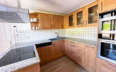 Cuisine en bois clair, avec des placards vitrés rappelant l'intérieur d'un voilier. Le plan de travail en granit et les appareils modernes complètent ce décor chaleureux.