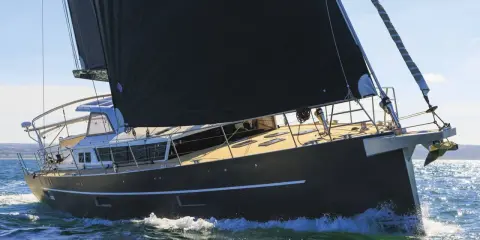 Un voilier moderne, avec une grande voile noire, navigue sur une mer agitée. Xavier Desmarest admire la vue depuis le pont.