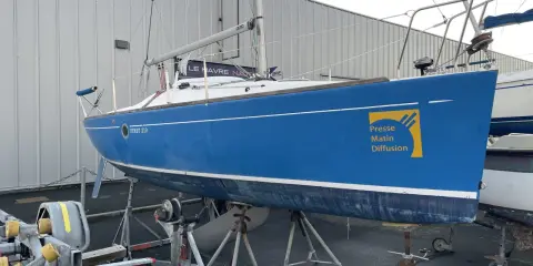 Voilier bleu FIRST 210 sur bers, prêt pour la saison. Le logo "Presse Matin Diffusion" est visible sur la coque.