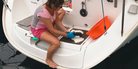 Préparation pour un tour du monde en voilier : une femme nettoie la plateforme arrière d'un bateau.