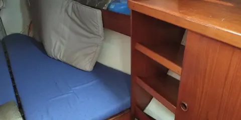 L'intérieur d'un voilier avec une couchette bleue, un coussin gris et des étagères en bois.