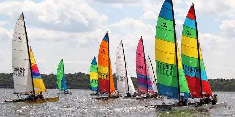 Course de Hobie Cat 18, voiles multicolores et blanches, sur l'eau par temps nuageux. Fiche technique du Hobie Cat 18.