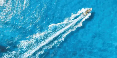 La coque d'un bateau fend les eaux bleues, laissant une traînée blanche de mousse.