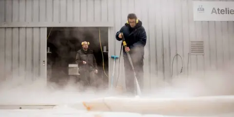 Deux hommes utilisent un nettoyeur haute pression pour nettoyer un voile de bateau avec du savon noir.